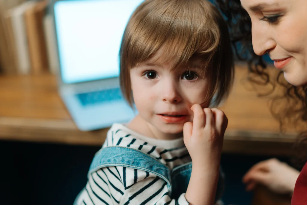 Copil timid lângă mama lui, care lucrează la laptop
